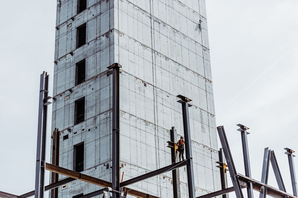 Photo of a construction worker standing on the large steel beam scaffolding of the future Center for Computing & Data Sciences building. The sky behind them is light blue.