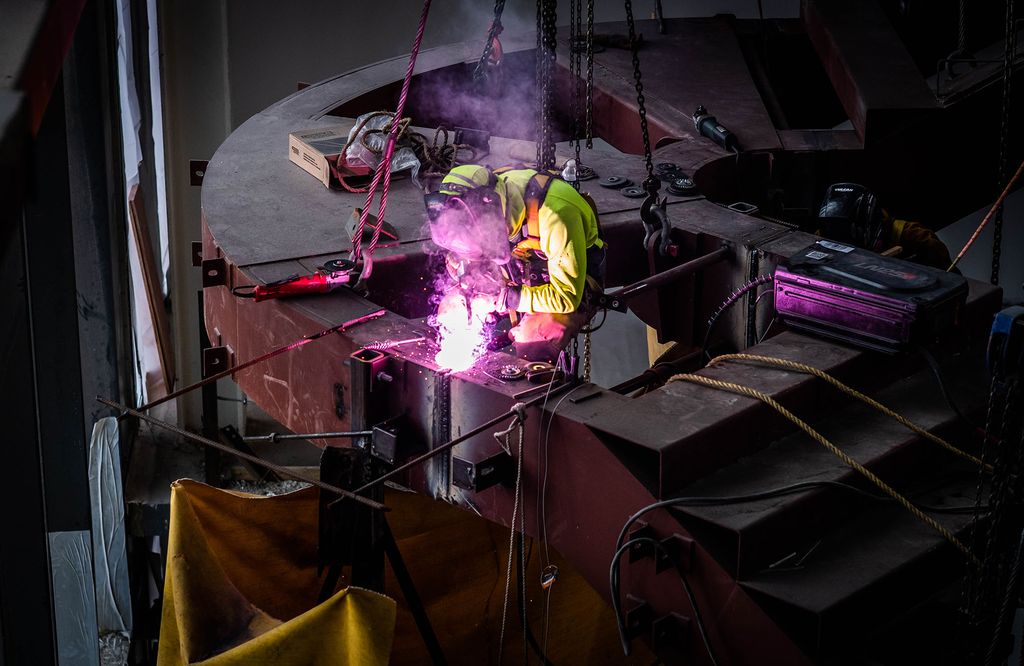 Photo: Installation begins on the staircase inside of The BU Center for Computing & Data Sciences on March 17, 2022. A construction worker welds in the dark on a staircase.