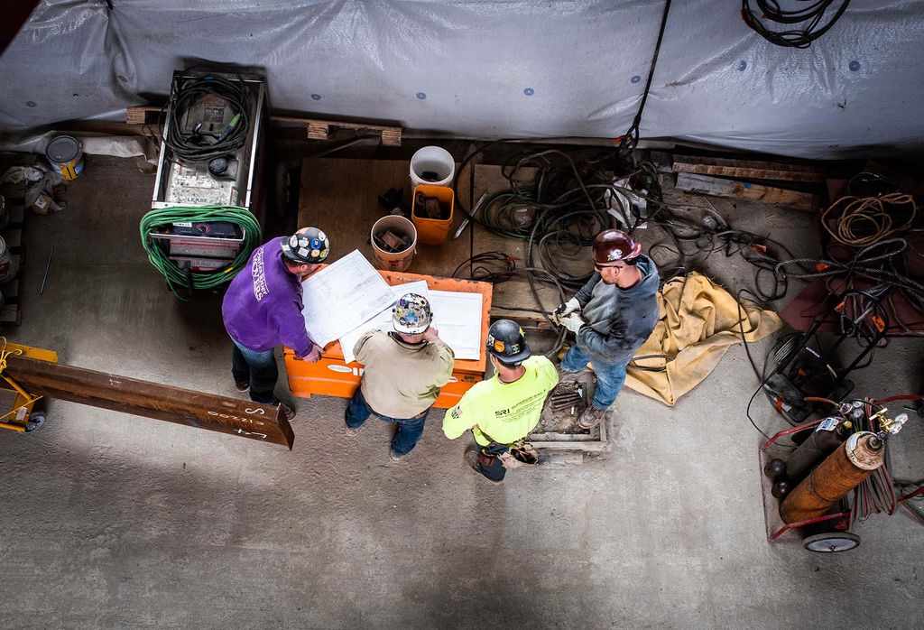 Photo: Installation begins on the staircase inside of The BU Center for Computing & Data Sciences on March 17, 2022. Overhead shot shows four construction workers reviewing a larger blueprint and plans.