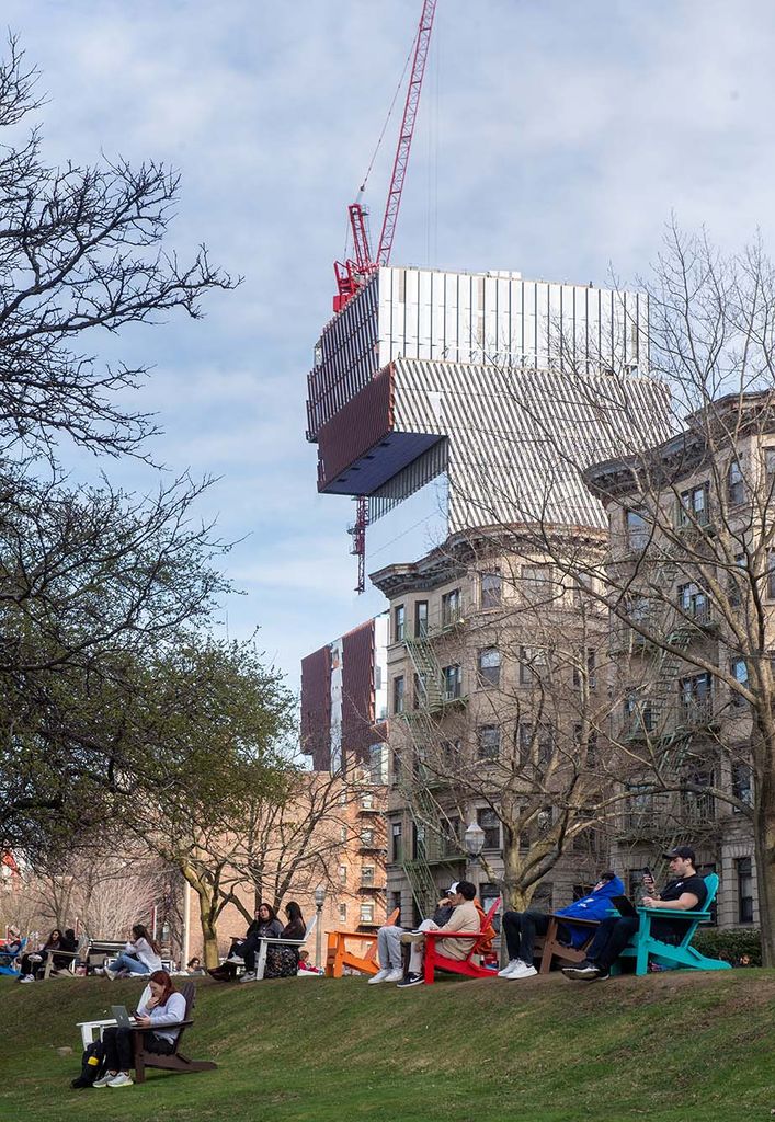 Photo: Students take advantage of a beautiful afternoon on BU Beach April 11.  A large crowd of students hang out on a green lawn. The Data Science building can be seen looming in the background with it's reflective mirror sides.