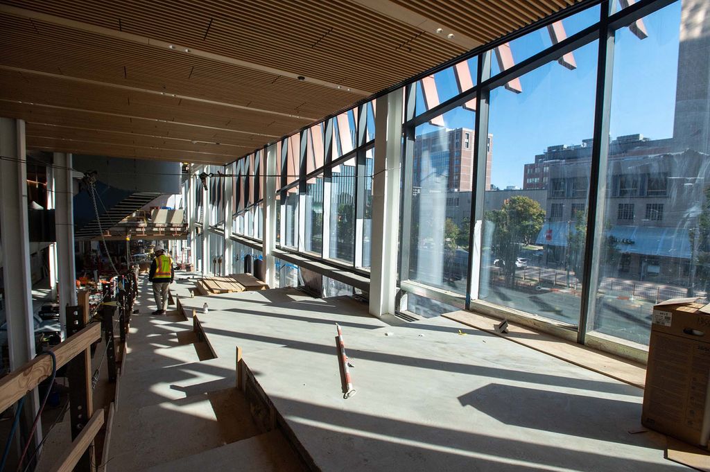 Photo: Interior of the Center for Computing and Data Science as work continues to be done. A large set of stairways set in cement are shown next to a large set of glass walls tot he right. Various construction workers can be seen working around the scene.