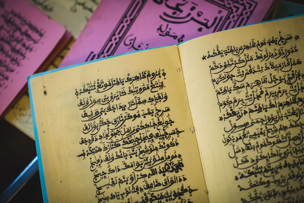 Photo: tan, pink, and blue books filled with, Ajami, a modified Arabic script, lay open on a table.