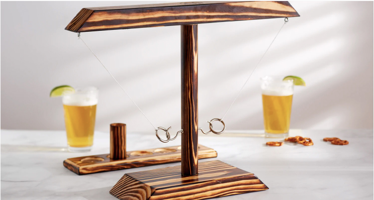 Photo: HOOKS!, the ring toss-beer pong hybrid apparatus is shown. A wooden structure with hooks attached to it is shown with two large glasses of beer shown in the background behind it.