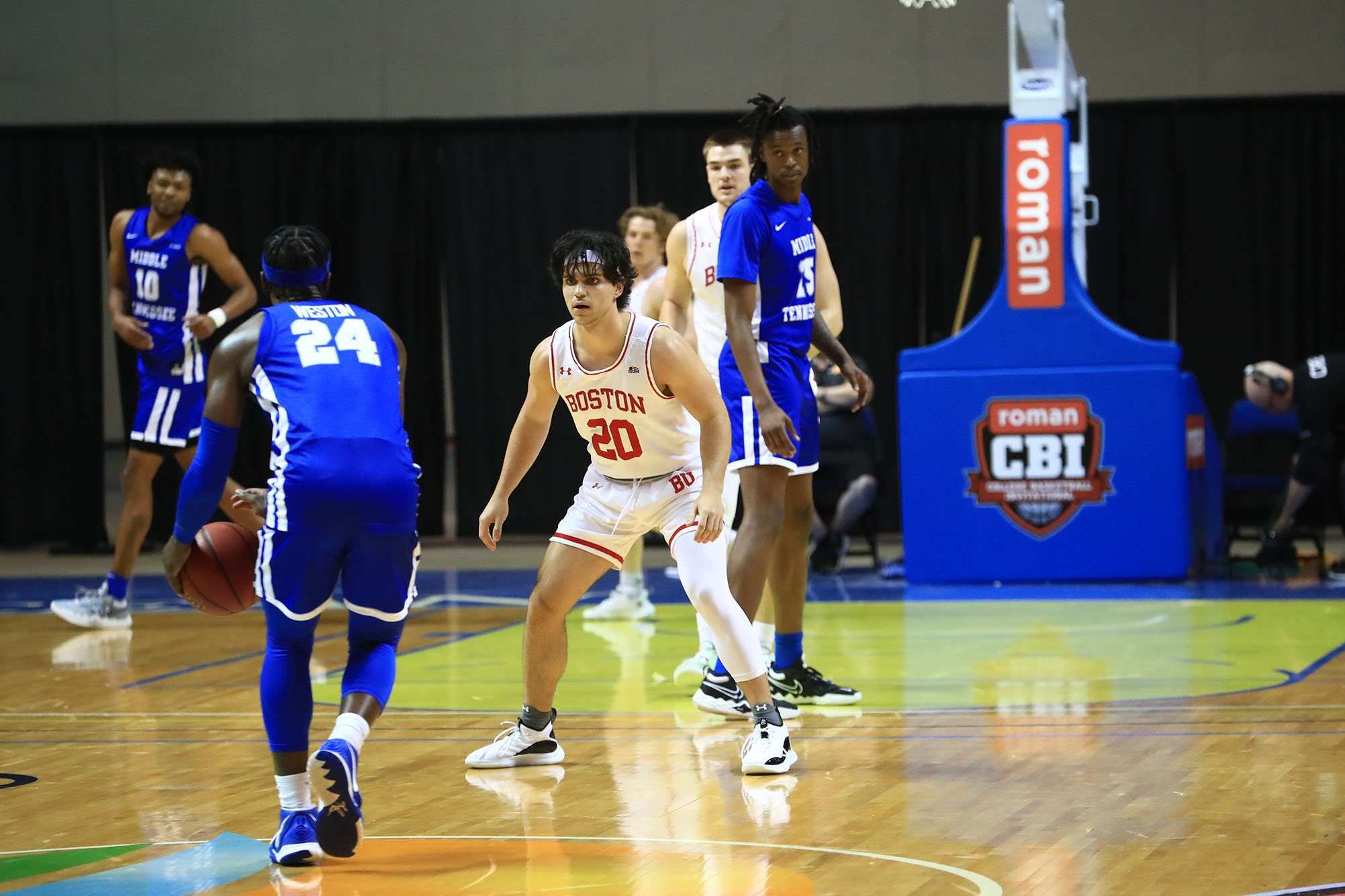 Photo: Jordan Tab (CAS’23, Questrom’23) playing against Middle Tennessee in the Roman College Basketball Invitational quarterfinal March 21, 2021. A tall, tan young man wearing a white and red BU men's basketball uniform defends on a basketball court against a player wearing a blue uniform and dribbling a basketball down the court.