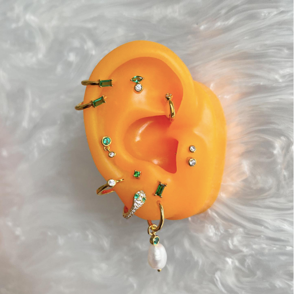 Photo: A fake bright orange ear model displays a variety of earrings, studs, and bars.