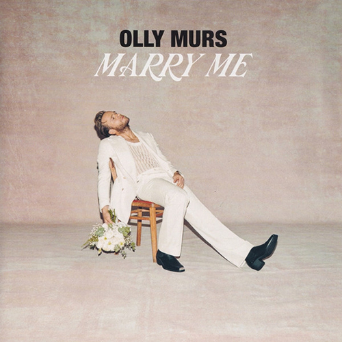 Album cover of "Marry Me" by Olly Murs. Olly, a white man wearing a white, sheer tank top, white pants, and white blazer, sits slumped backwards in a chair in a blush-colored room. One hand holds a white bouquet. Cover reads "Olly Murs, Marry Me".