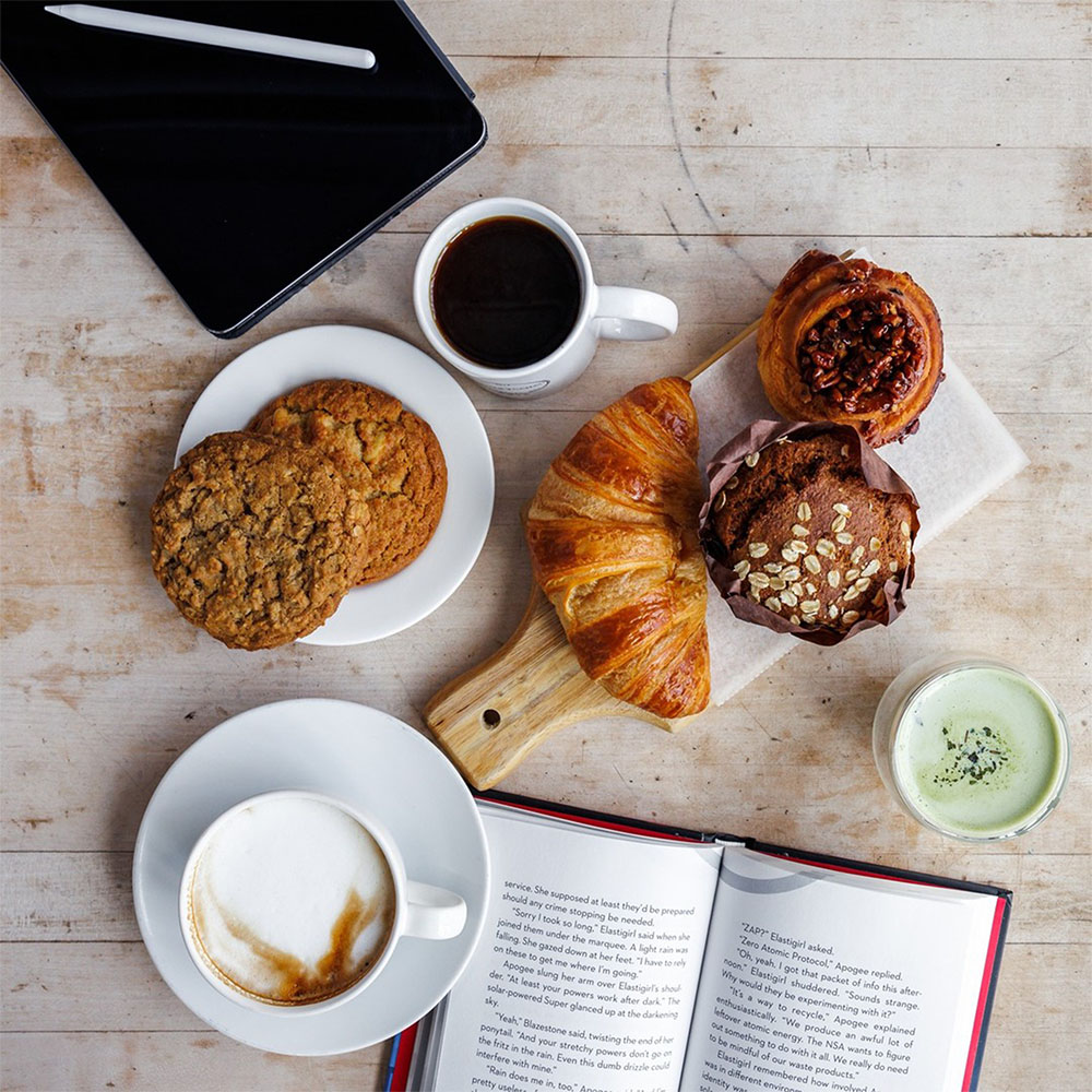 A table at the Dudley Cafe containing cookies, a croissant, coffee, and more