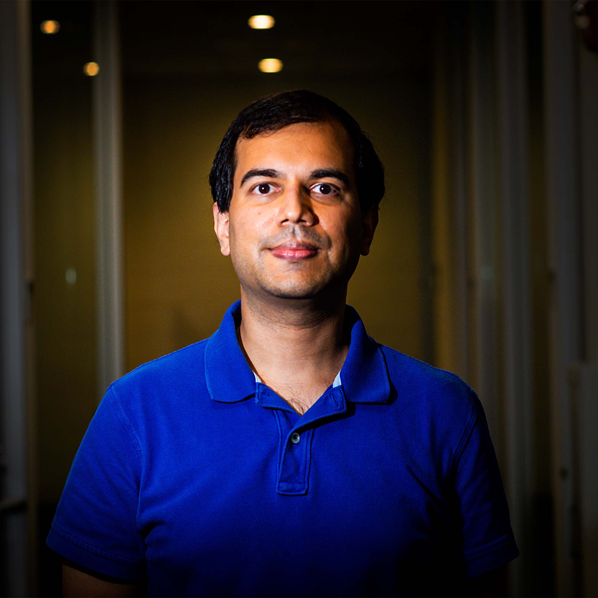 Mayank Varia portrait on a dark background in a blue shirt