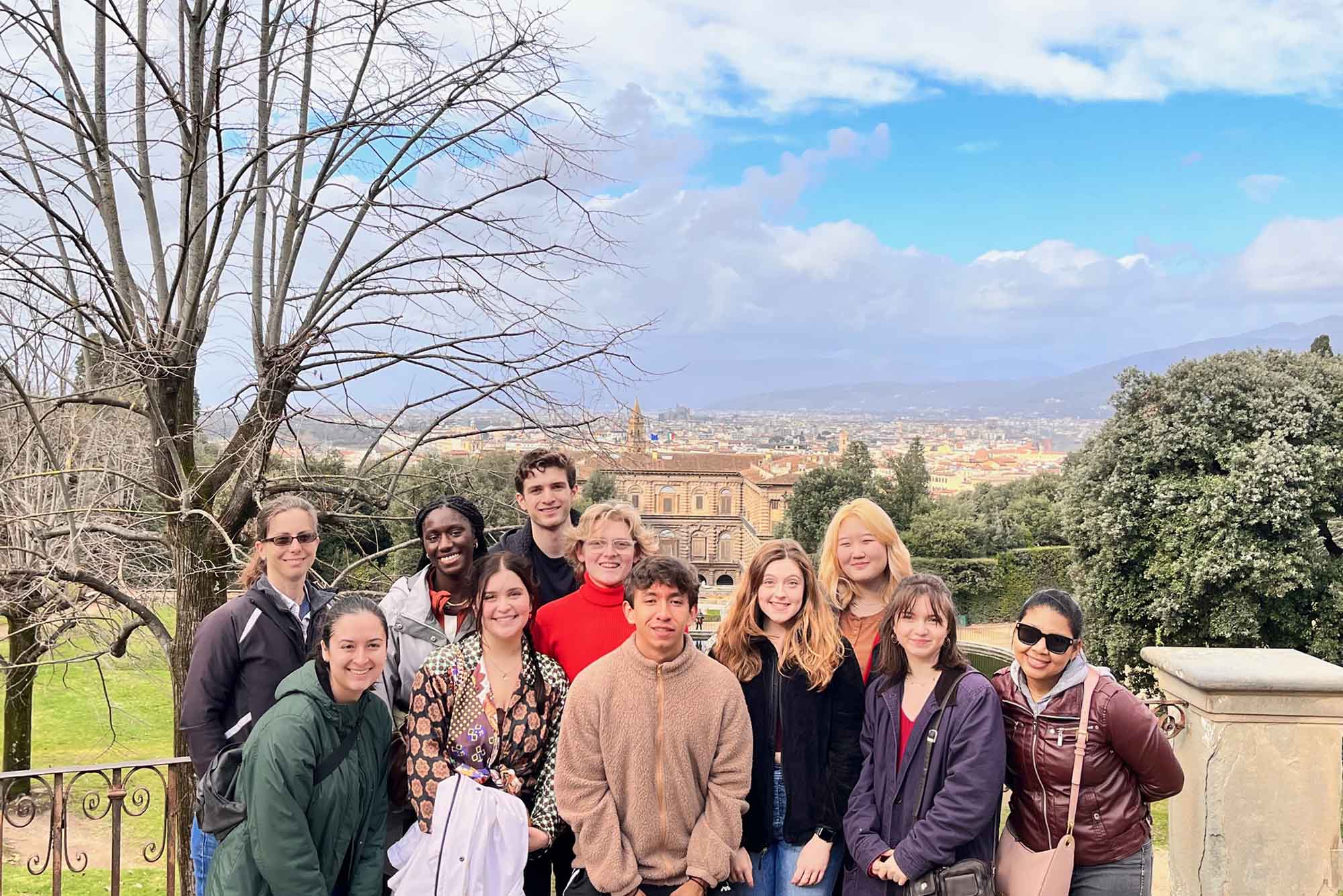 Photo: A group of students dressed in jackets and cold gear smile for the camera on a sunny, partly cloudy day. Distant buildings can be seen behind them.