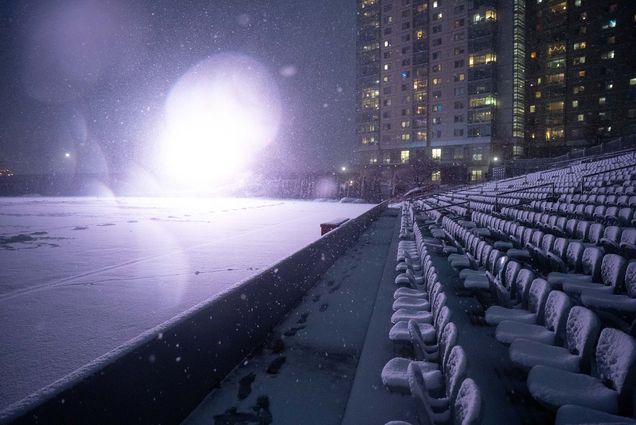 Photo: Snow falls on Nickerson Field on the evening of Jan 23. The nighttime seen shows a large apartment building in the background as the stands and soccer field accumulate snow. The field lights shine brightly on the snow creating a scenic snow showcase.