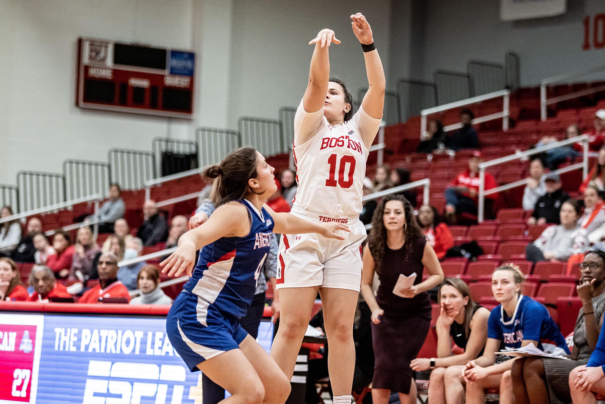BU Sophomore Alex Giannaros takes a shot against American on January 8, 2023. Two women playing basketball, one shoots a 3 point shot over the other at an indoor basketball court.