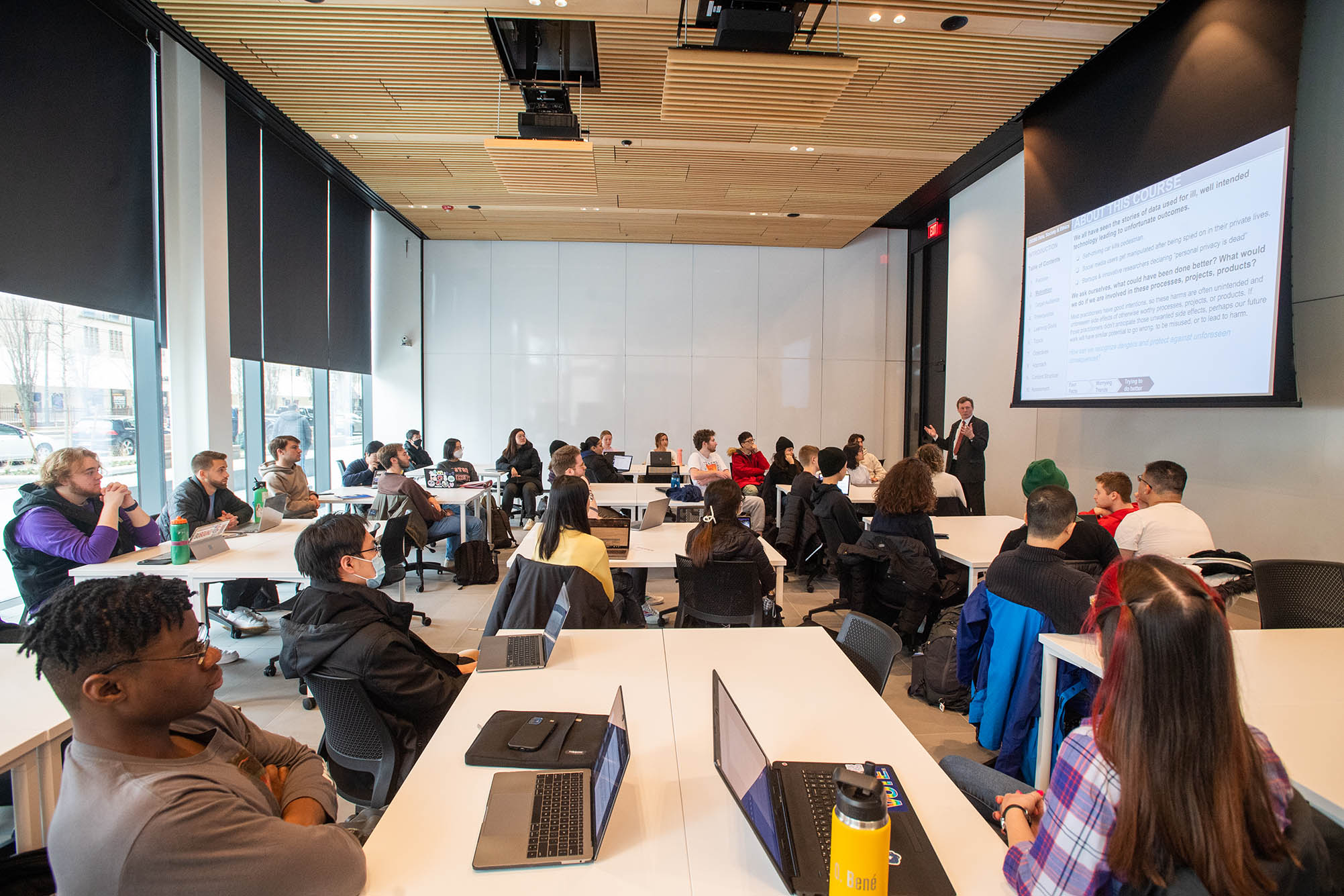 Photo: STH professor Wesley Wildman’s ethics class taking place in a first floor classroom in the Center for Computing & Data Sciences on January 19. A professor stands at the front of an airy, bright classroom as students sit before them at long wooden tables.