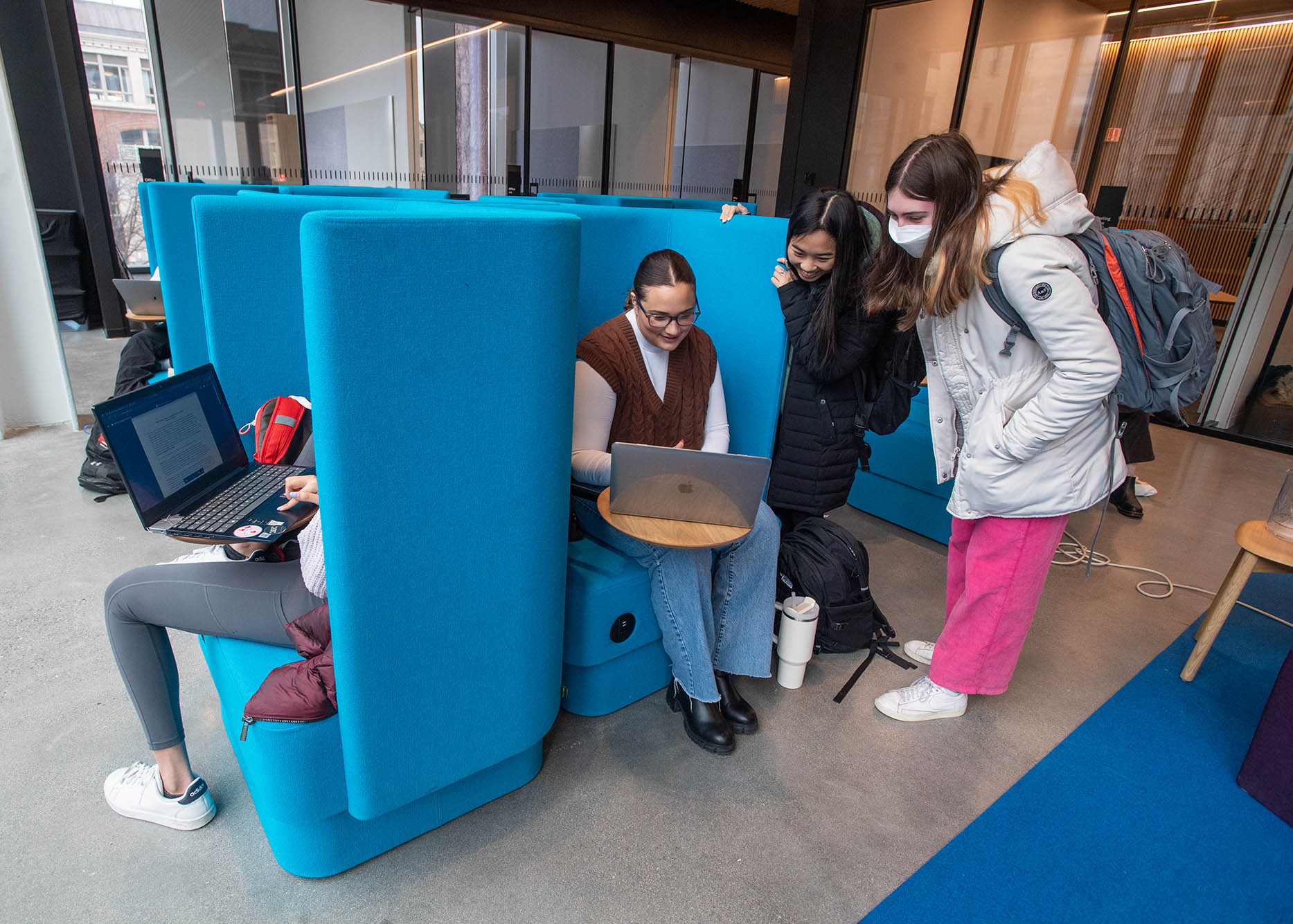 Photo: Becky Geisberg (CAS’26), center from left, Ella Hain (CAS’26), and Amelia Liston (CAS’26) chat for bit at SPARK on the second floor of the Center for Computing & Data Sciences on January 19. Three young women, one seated in a large blue chair and the others standing beside her, look at a singular laptop screen.