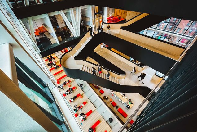 Photo: Overhead shot of students walking and gathering in and around a large set of black and wood butterfly stairs.