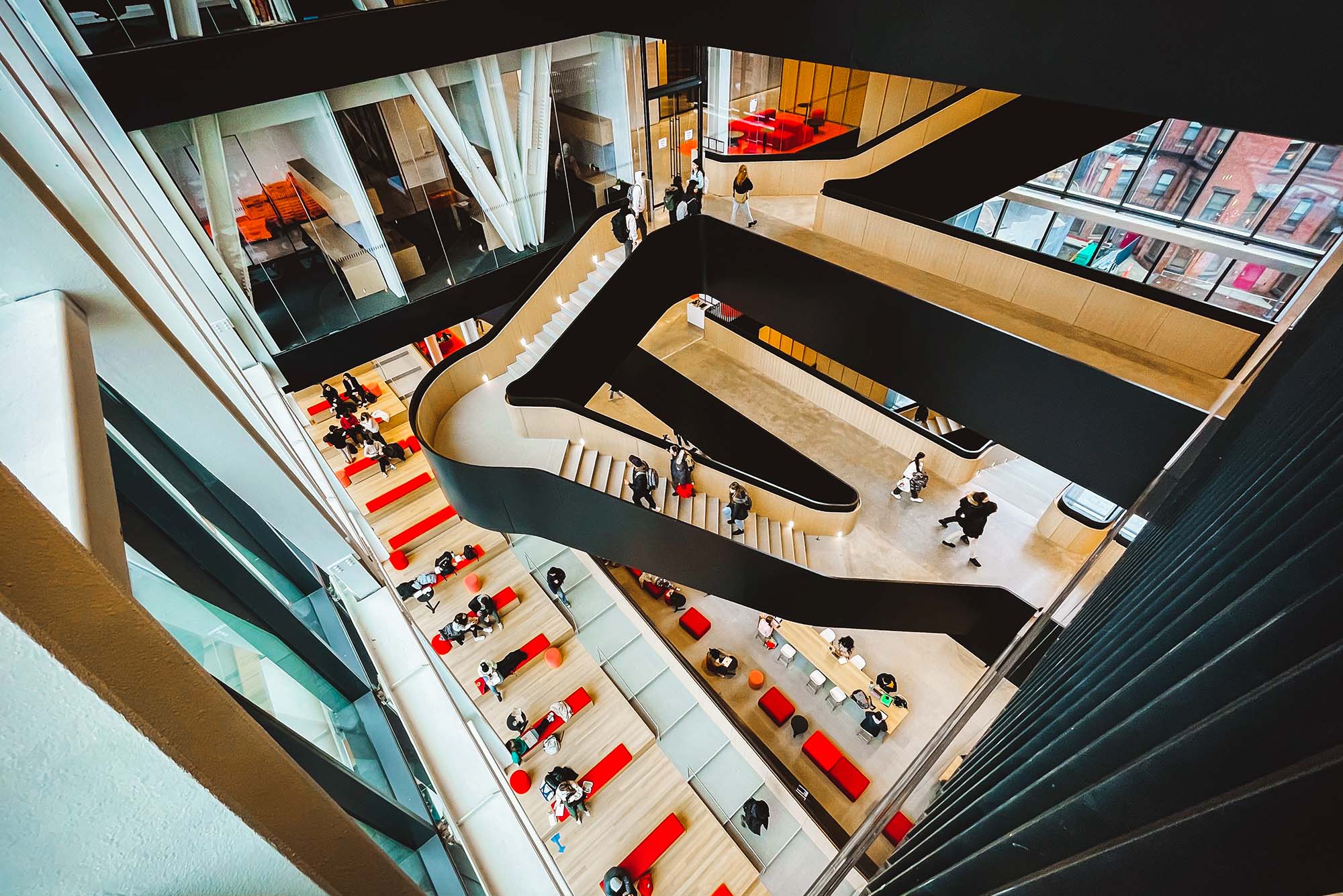 Photo: Overhead shot of students walking and gathering in and around a large set of black and wood butterfly stairs.