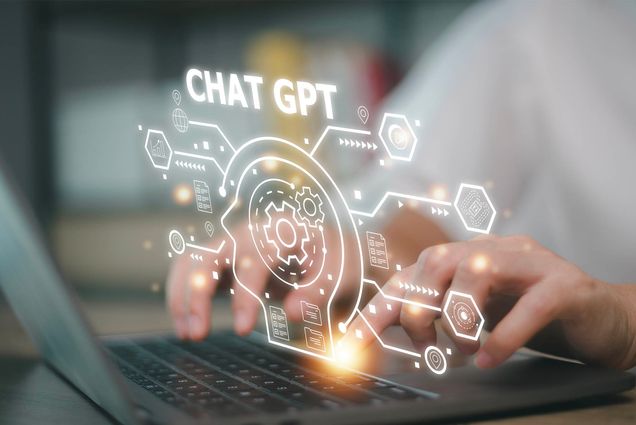 A photo of a person sitting at a laptop typing, with a virtual reality overlay popping out of the screen depicting a robot head and many glowing lines and shapes. Photo by iStock/Userba011d64_201