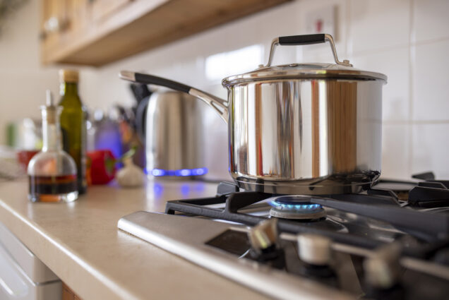 Photo: Close-up side-view shot of a cooking pot on a gas stove. Various kitchen appliances can also be seen on the counter in the background.