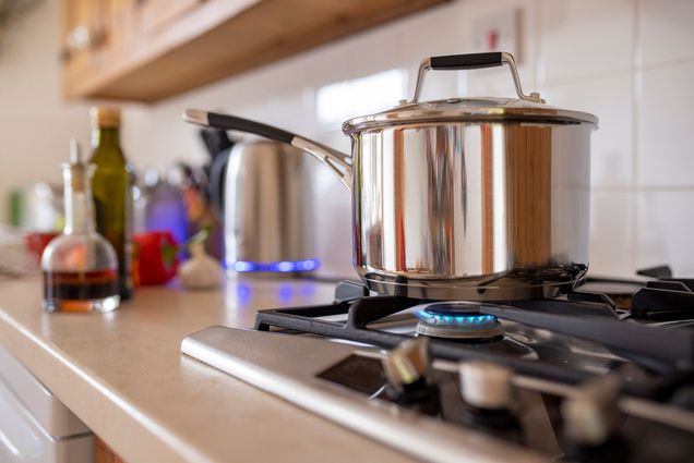 Photo: Close-up side-view shot of a cooking pot on a gas stove. Various kitchen appliances can also be seen on the counter in the background.