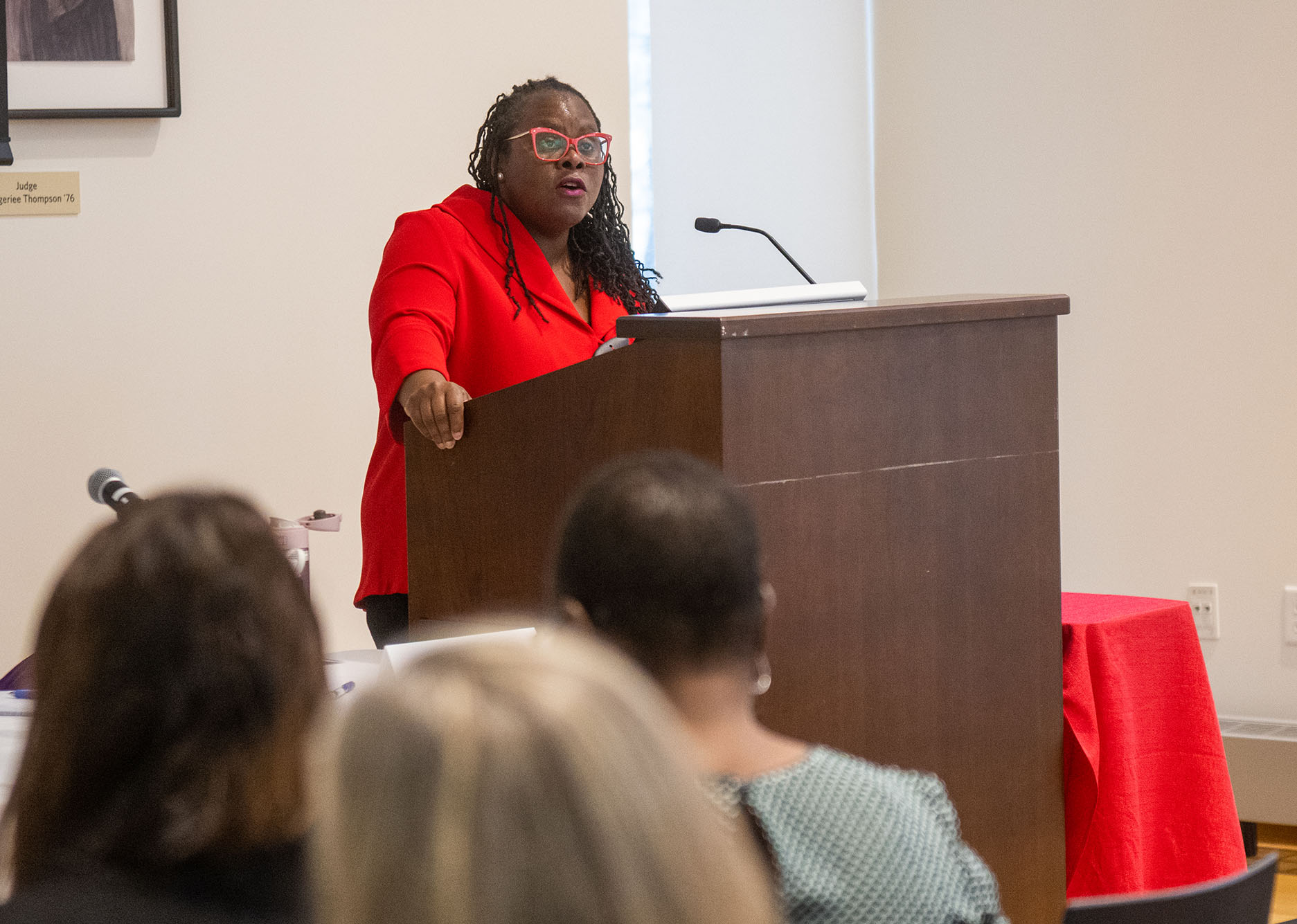 Photo: LAW Dean Angela Onwuachi-Willig at After Roe and Dobbs: Seeking Reproductive Justice in the Next Fifty Years. A Black woman with long, black dreadlocks and wearing glasses, a red blazer, and black pants, stands at a wooden podium and speaks to an audience seated in chairs in front of her.