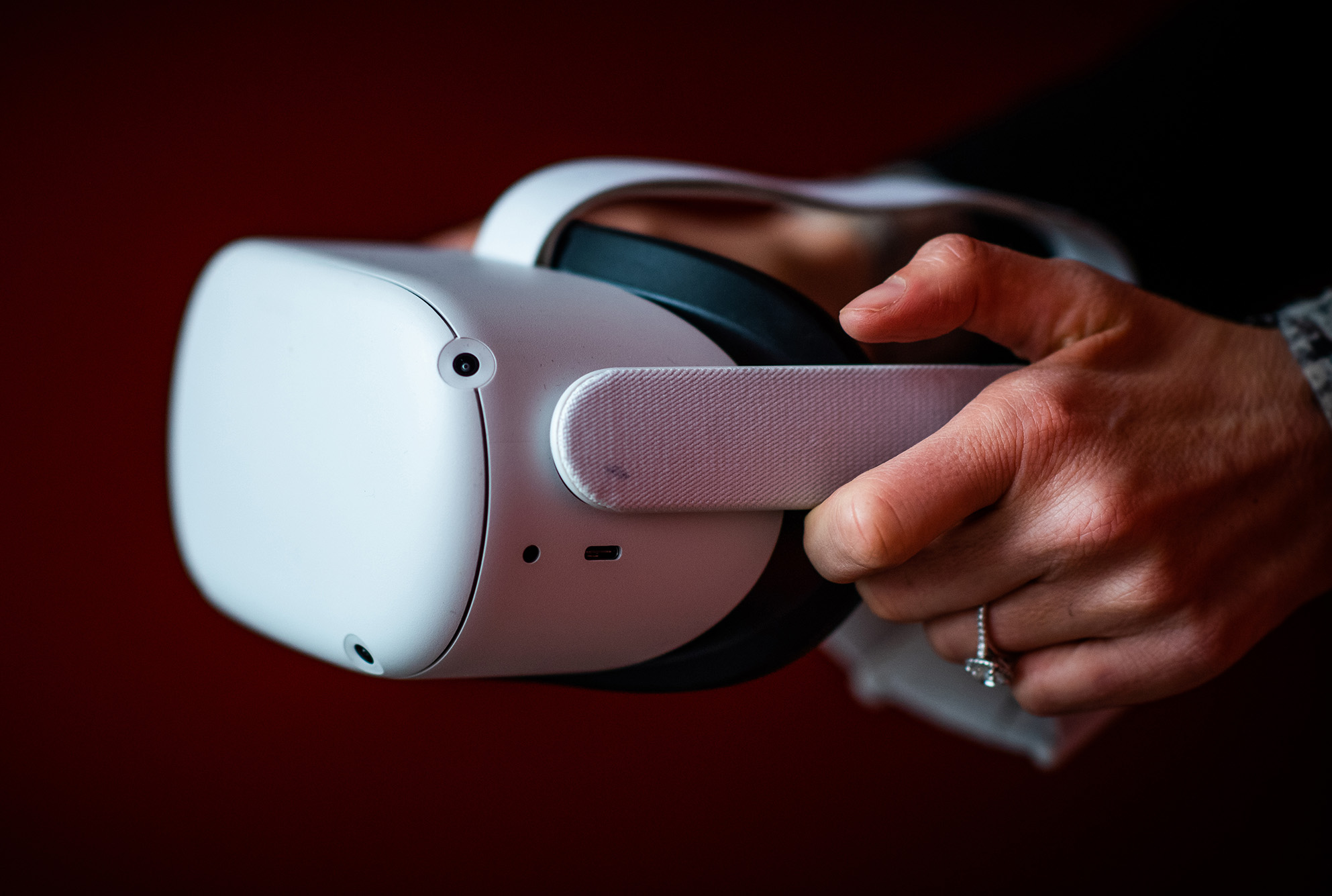 Photo: Two hands hold up a white VR headset in front of a dark red wall.