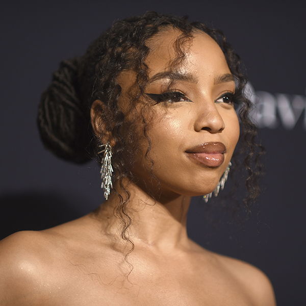 Photo of Chloe Bailey, a light-skinned, young Black woman, posing on a red carpet, with curly hair brown dreadlocks formed into a stylish bun.