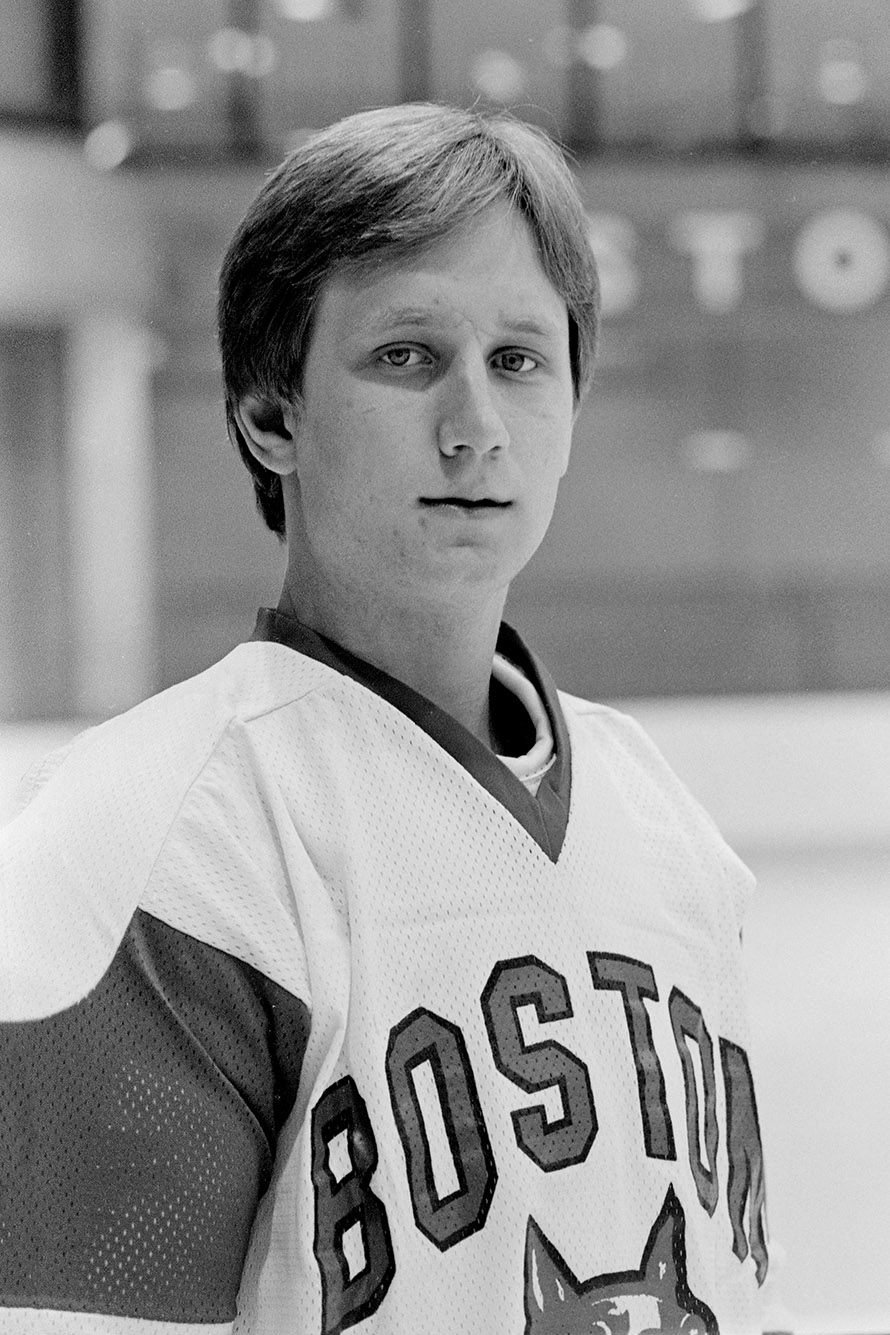 Photo: Black and white photo of a young white man wearing a Boston university men's ice hockey uniform. He poses on the ice for a headshot photo.