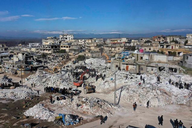 Photo: Rescuers and residents search through the rubble of collapsed buildings in the town of Harem near the Turkish border, Idlib province, Syria, Wednesday, Feb. 8, 2023. Overhead shot of collapsed building, rubble, and people.