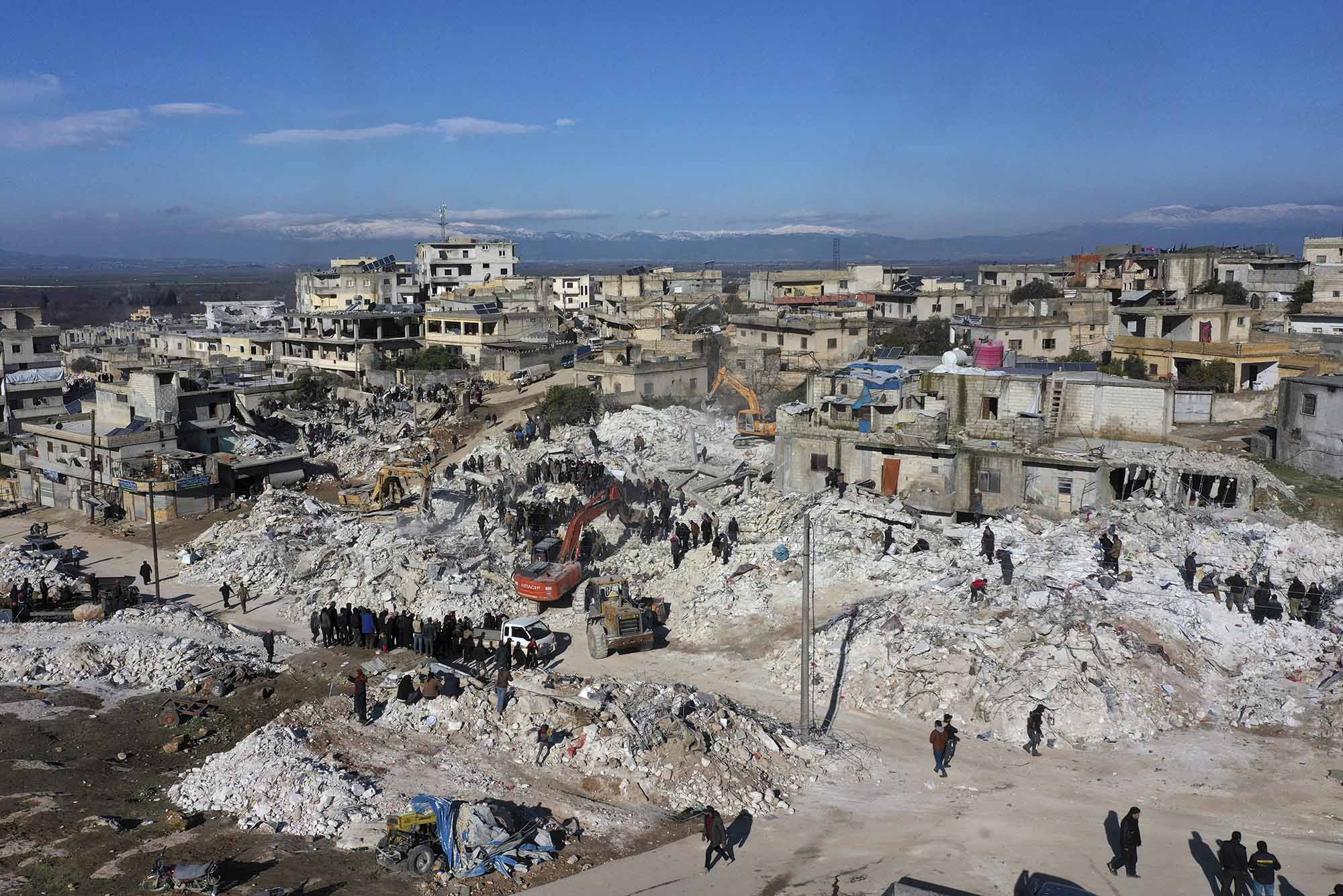 Photo: Rescuers and residents search through the rubble of collapsed buildings in the town of Harem near the Turkish border, Idlib province, Syria, Wednesday, Feb. 8, 2023. Overhead shot of collapsed building, rubble, and people.