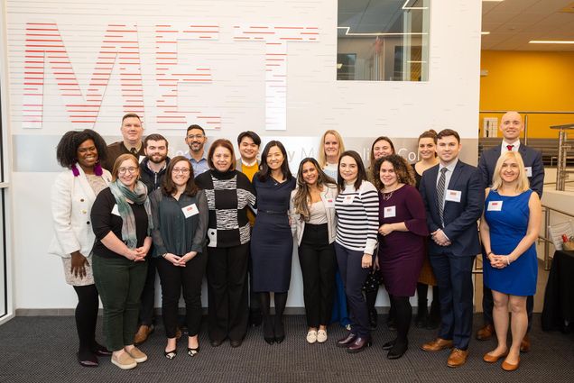 Photo: Boston Mayor Michelle Wu poses for a group picture with the 12th Annual City of Boston Scholar recipients during the recognition event at Metropolitan College, Thursday, February 9, 2023. A diverse group of people pose in front of a large, tan wall that has the letters "MET" in red behind them.