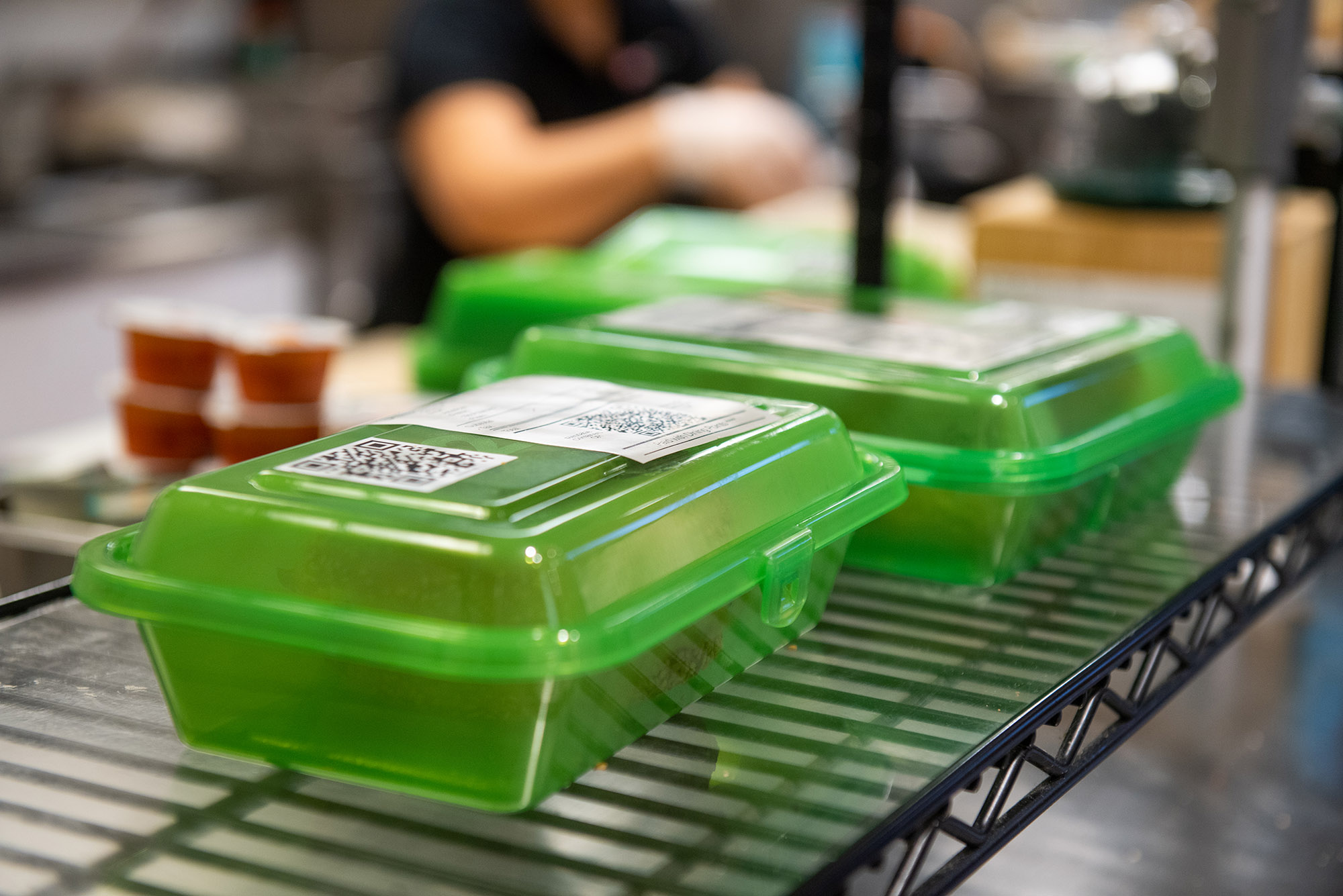 Photo: Clear green to-go containers are shown with orders in them on wire racks. They're each labeled with receipts for what is in the order.