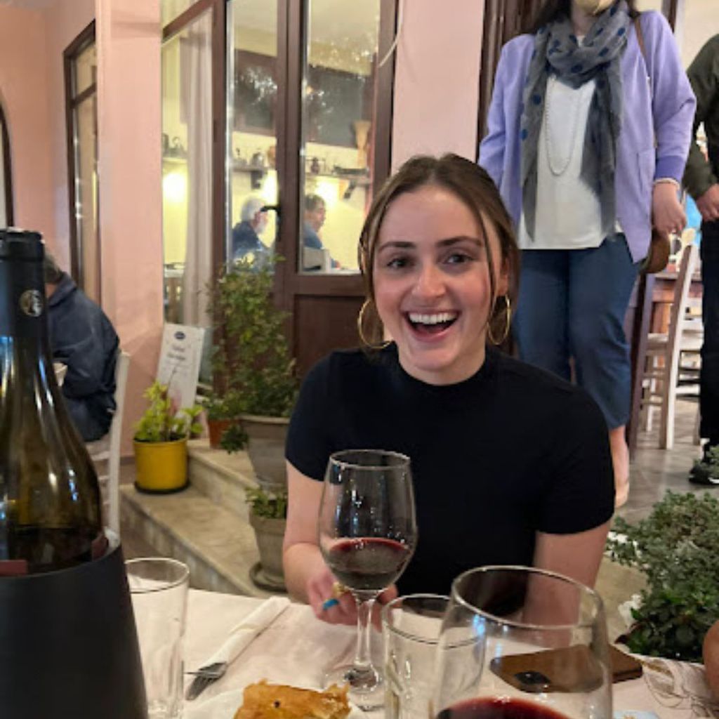 Student, Samantha Ruh, is pictured sitting at an outdoor restaurant with a big smile on her face. 
Picture credit: Samantha Ruh (SHA'23)