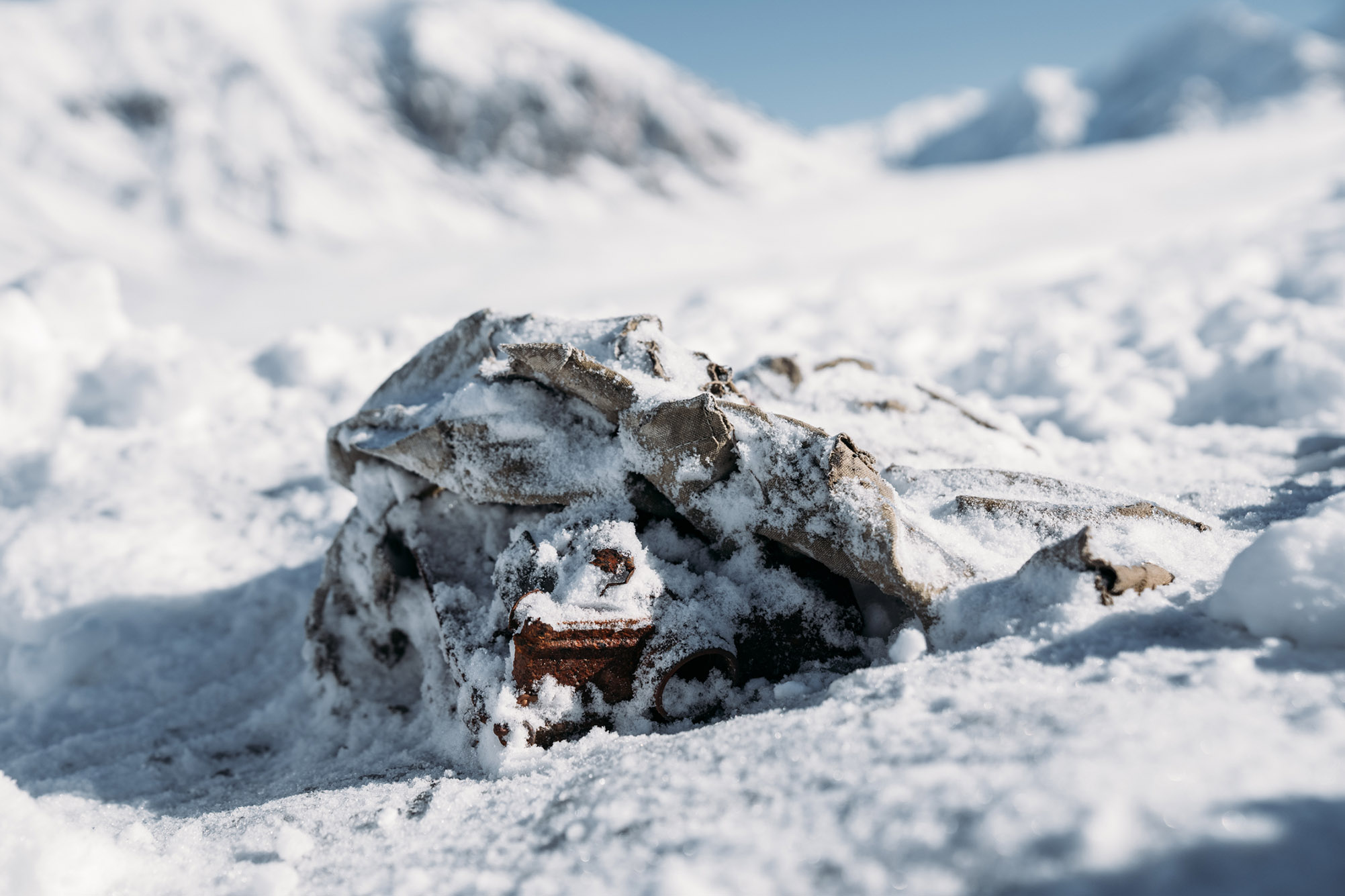 Photo: Closeup of a dark brown leather satchel buried in a bank of snow. Mountain tops can be seen in the blurry background.