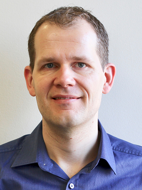 Photo: Headshot of Michael Holm. A white man wearing a blue collared shirt smiles and looks toward the camera.