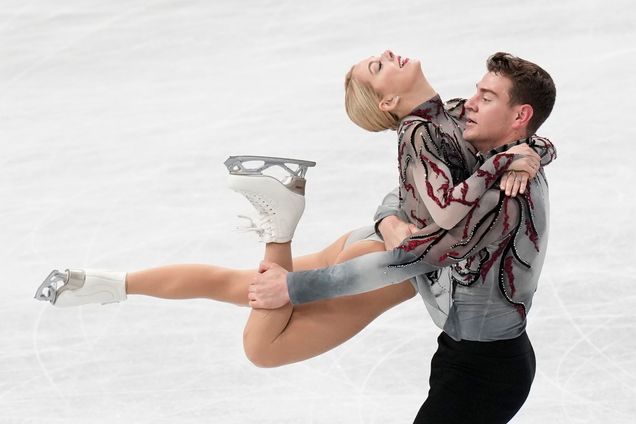 Photo: Alexa Knierim and Brandon Frazier of the U.S. perform during the pairs' short program in the World Figure Skating Championships in Saitama, Wednesday, March 22, 2023. A tall, white man wearing a grey and red themed figure skating outfit holds up a white woman with a similarly-styled figure skating outfit by her knee. They both have dramatic looks on their faces as they skate on the ice.