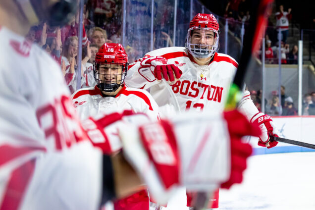 Photo: Two BU players smile in the camera as they come back to the bench. They wear their white and red uniform.