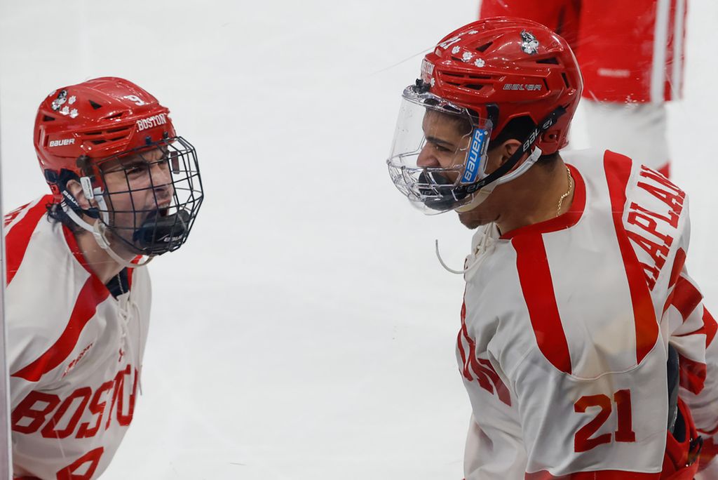 Photo: Two BU hockey players scream in excitement after winning 10th title at Hockey East. They wear their white uniform with red lettering.