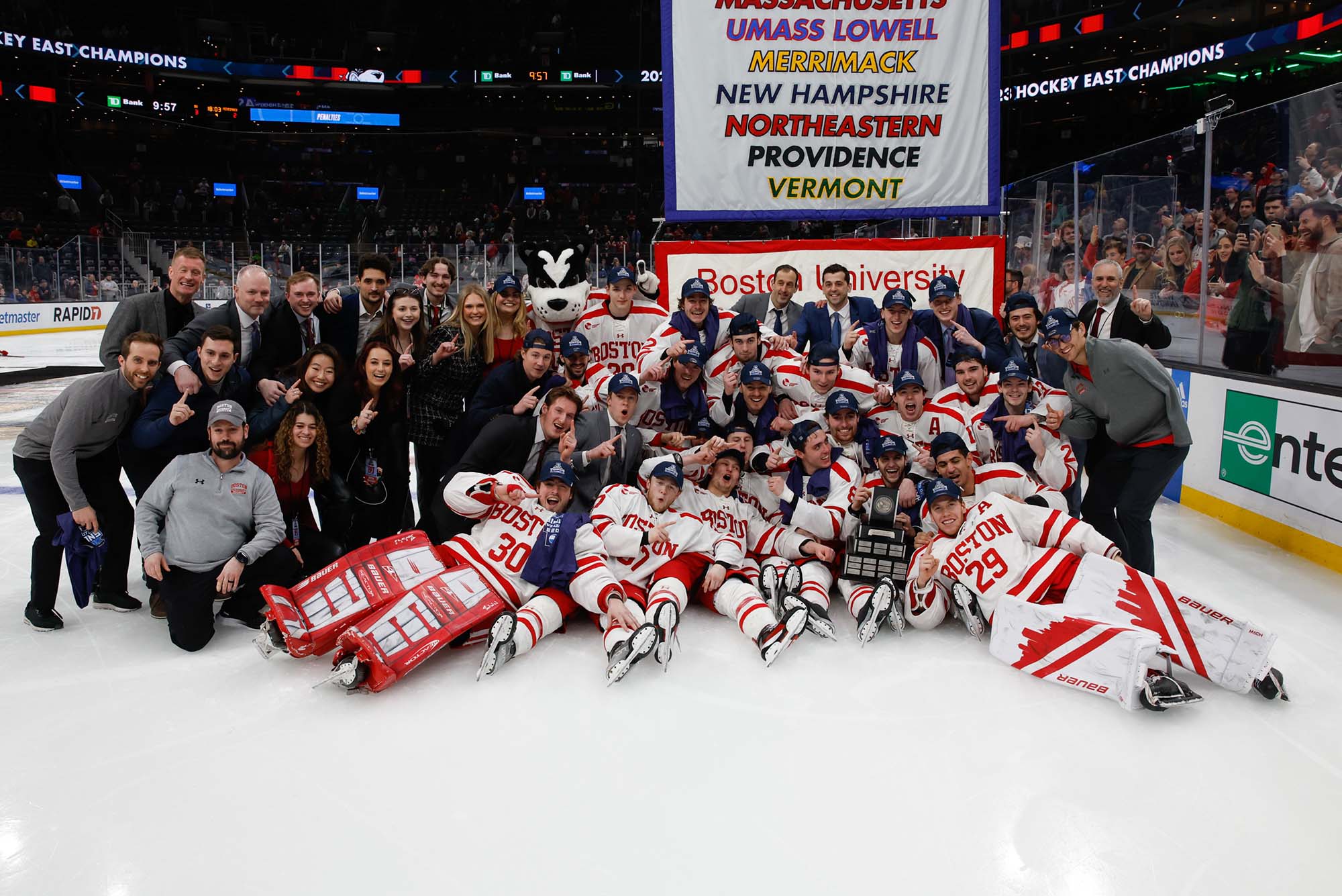 Photo: The entire BU Men's Hockey team pose in celebration after winning their 10th Hockey East championship. The staff are in all black while the players are in their white with red detailing uniform.