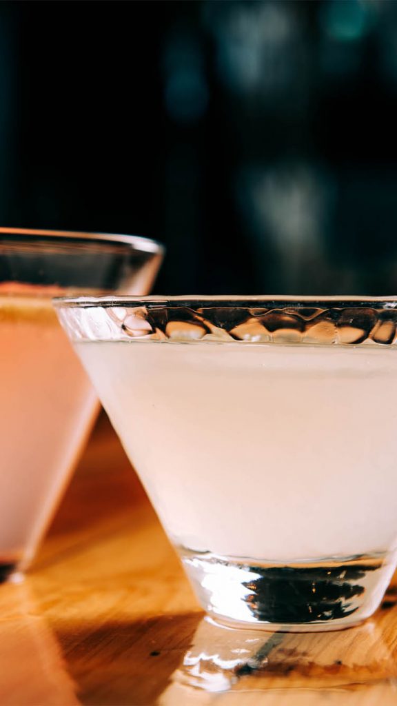 Two glasses filled with mixed alcoholic drinks on a wooden bar top