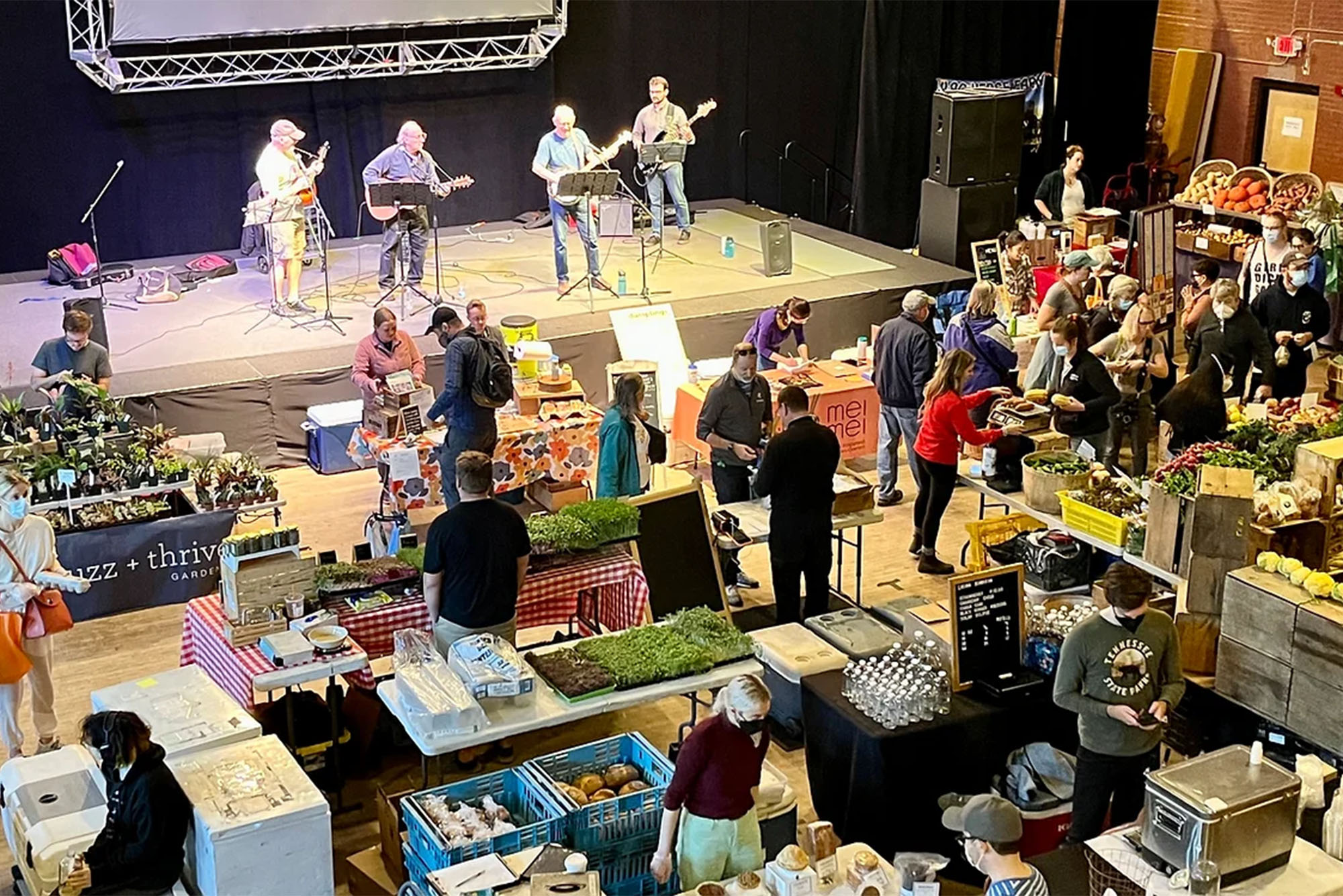 a large group of people watching a musical performance by a 4 member band at a farmers market in Somerville, MA