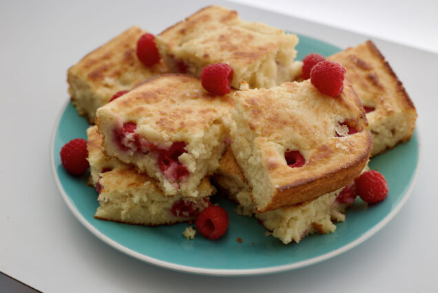 Photo: A plate of golden, fluffy pancakes decorated with red raspberries. The plate is Tiffany blue and the fluffy pancakes are cut into squares.