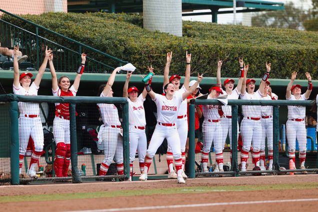 Photo: The BU Women's Softball team, wearing white and red jerseys, celebrates in the dugout during a recent game