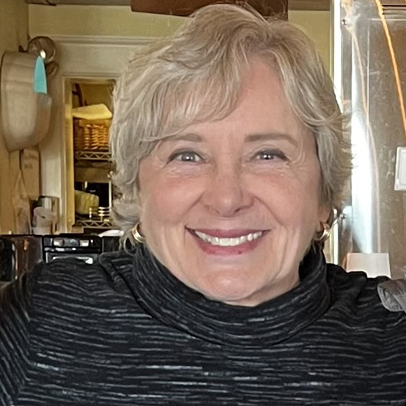 Photo: A white woman with short, brown-gray hair and wearing a black, relaxed turtleneck smiles and poses for the camera.