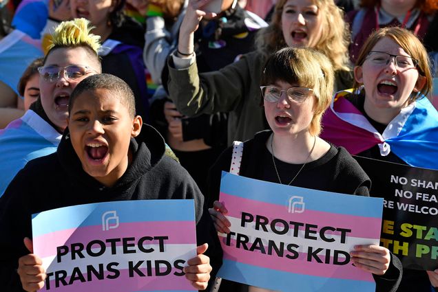 Photo: Protesters of Kentucky Senate bill SB150, known as the Transgender Health Bill, cheer on speakers during a rally on the lawn of the Kentucky State Capitol in Frankfort, Ky., Wednesday, March 29, 2023. A group of young people yell and hold signs of the light blue, pink, and white striped transgender flag. The signs read "Protect trans kids"