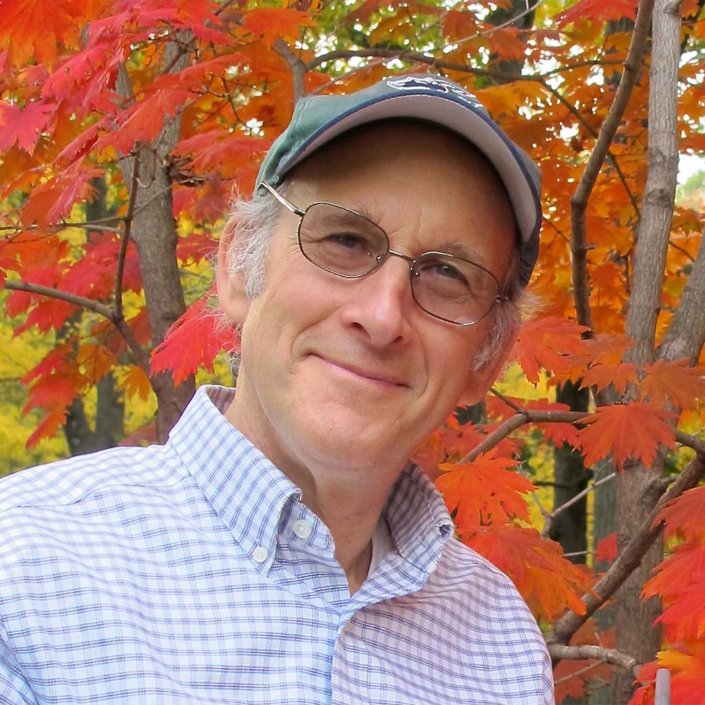 Photo: Portrait headshot of Richard Primack, a white man wearing glasses, a cap and a collared shirt