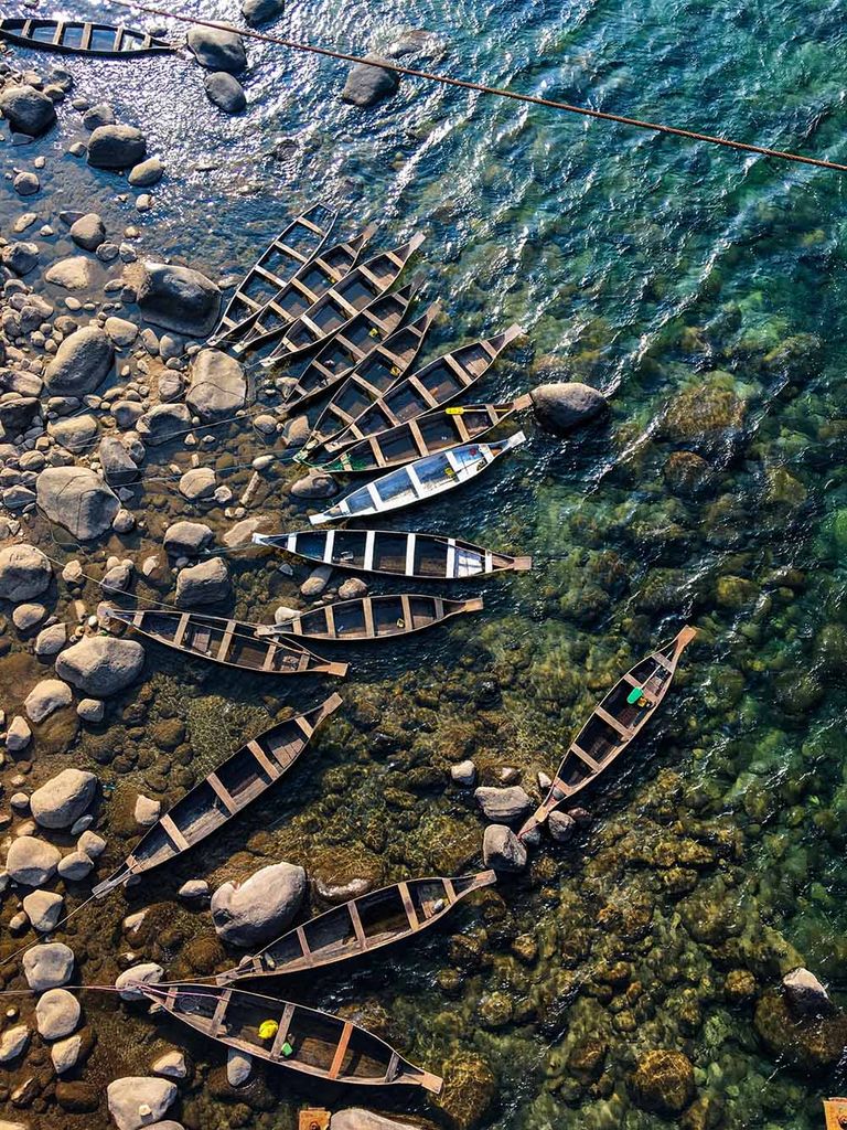 Photo: Overhead shot of small boats docked to the rocky shore of the Umngot river. The water is so clear the rocks on the sea floor can also be seen.