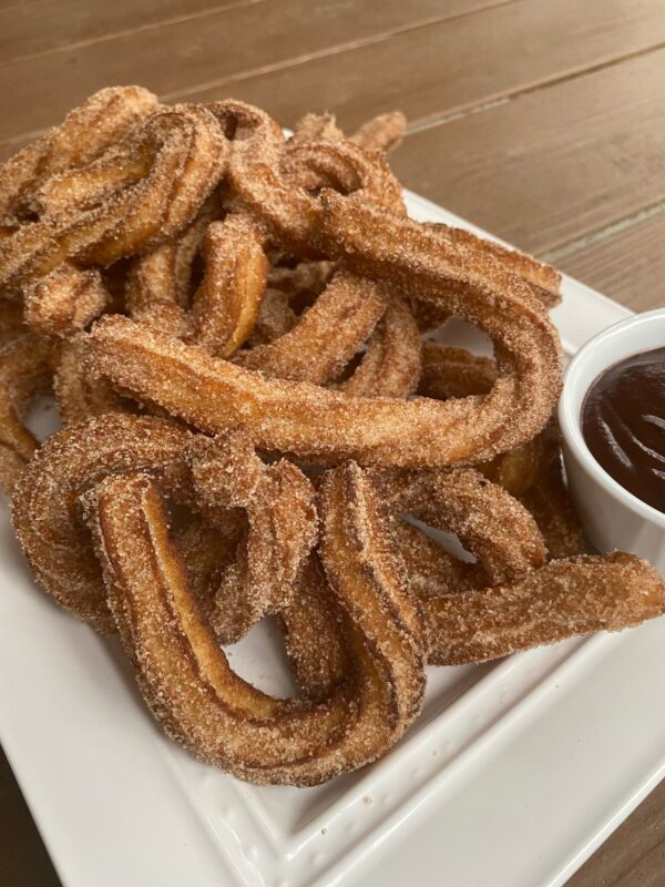 Photo: a plate of churros, a fried dough covered in cinnamon sugar, with a side of chocolate dipping sauce.