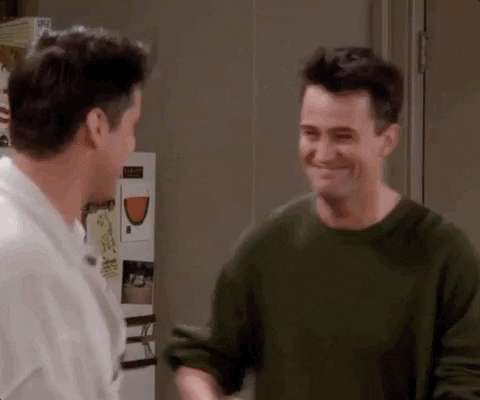 This is a GIF from the TV show Friends. It shows two male characters embracing each other while smiling. They are in an apartment. They pat each others backs while in the hugging embrace.