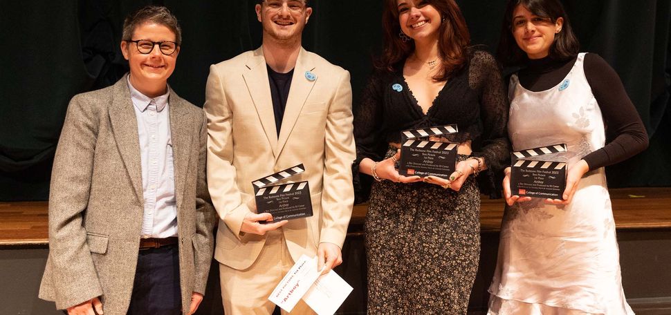 Photo: A group shot of the winners of the Redstone Film Festival. From left, a short white man in a gray blazer and a blue button-up dress shirt. Next, a taller Southern Asian man in a stream-lined tan suit and a black t-shirt. Next to him, a Southern Asian woman in a black, lace top and a floral maxi skirt. And lastly, the person on the right is a Sourthern Asian woman with a black mock-neck top and a silk, grey dress.