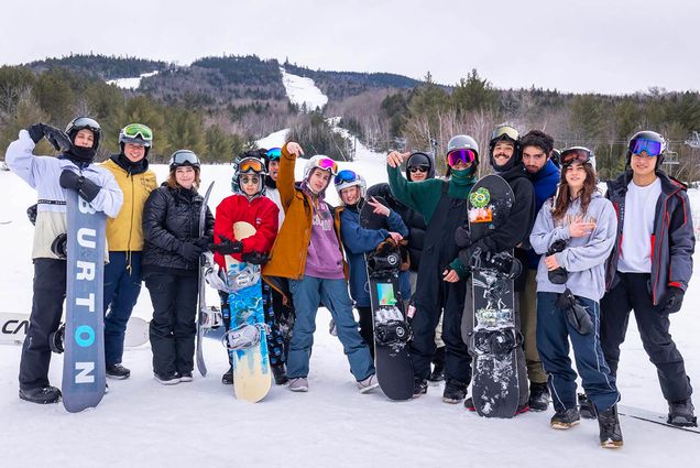 Photo: A panned shot of the entire BU snowboarding team on a snow slope. They are all in their personal gear and warm clothes.