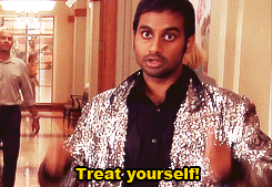 This is a Gif from the show 'Parks and Recreation' where on one of the characters is looking at the camera and pointing with both hands saying "treat yourself!" He is wearing a sparkly blazer and a black shirt and is in an office building. There are other people walking behind him. There is a caption that says "Treat yourself!" at the bottom of the image in yellow lettering. 